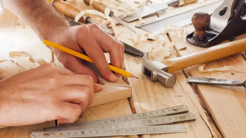 Artisan traçant une mesure au crayon sur une pièce de bois, précision du calcul