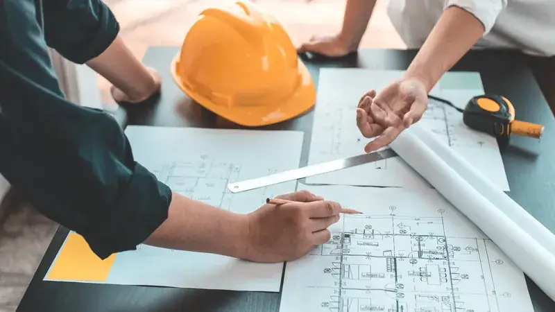 Mains sur des plans avec casque de chantier et mètre, travail de bureau